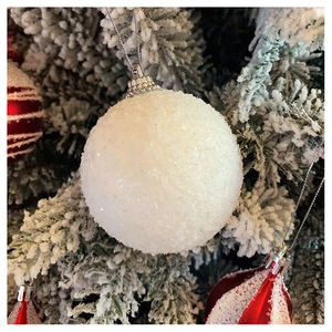 Detailed view of white snowy Christmas ball with glitter texture on a festive pine branch