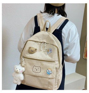 Vista trasera de una mochila de pana beige con parches de ositos y un amuleto de peluche