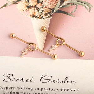 Detail of two golden industrial barbell earrings with zircon cross pendants on a pink surface