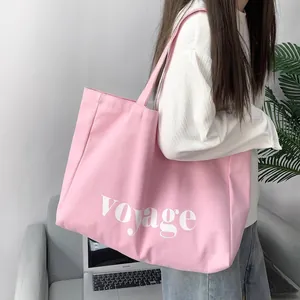 Close-up of pink canvas tote bag featuring white voyage text on a shoulder strap model