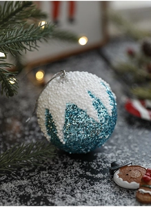 Macro d'une boule de Noël bleue scintillante avec neige en mousse et lumières chaudes