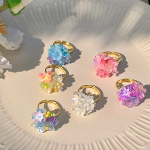 Detail of colorful resin beaded flower rings with adjustable gold bands on a ceramic tray