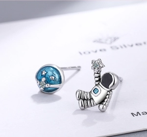 Macro detail of asymmetric astronaut earrings with starry blue enamel and sparkling stones