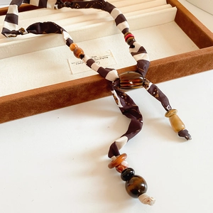 Detail view of ethnic fabric cord necklace with tiger eye beads and amber resin accents