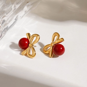 Gros plan de boucles d'oreilles nœud vintage dorées avec perle rouge sur marbre