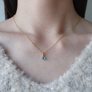Dettaglio di un ciondolo con pietra blu su catena d'oro indossato da una modella