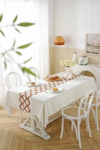 Detail of embroidered geometric lattice tablecloth with tassels on a wooden dining table