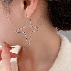 Close-up of minimalist silver four-point star earrings worn by a model in a soft setting