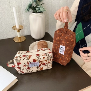 Détail d'une trousse à maquillage en velours côtelé avec imprimé floral et dragonne latérale