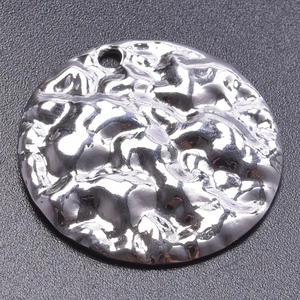 Detail of round silver pendant with irregular hammered texture and metallic finish