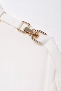 Detail view of the golden metal buckle and crepe fabric shoulder strap on white shirt