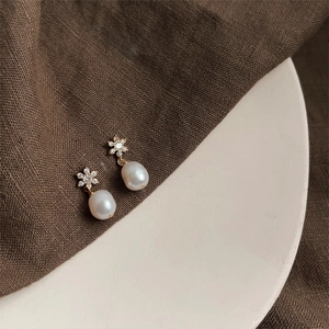 Macro detail of baroque pearl earrings with zircon floral studs on a ceramic tray