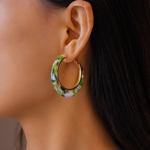 Close-up of a model wearing large C-shaped acetate hoop earrings with colorful marble pattern