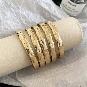 Detail of five hammered gold bangles displayed on a minimalist cream jewelry stand