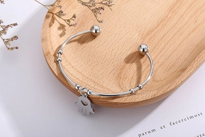 Detailed view of a silver Hamsa hand open bangle placed on a natural wooden display tray