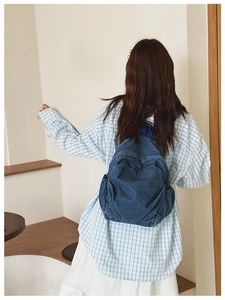 Rear view of a model wearing a small blue denim backpack with front zipper pocket detail