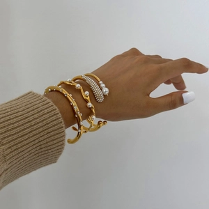 Detailed close-up of three gold-plated open bangles with pearls and crystals on wrist