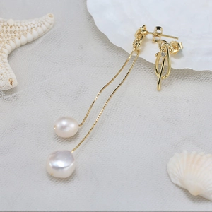 Detail showing elegant gold drop earrings with white pearls and knot design on seashells