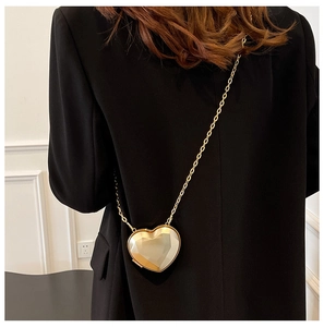 Detail of a mini gold heart-shaped evening bag with a metal chain worn on a black blazer