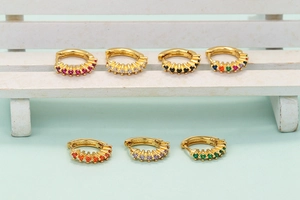 Detail of seven gold-plated hoop earrings with colorful zircon stones on a mini chair