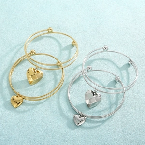 Detail of gold and silver double-layered wire bracelets with heart charms on blue fabric