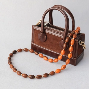 Détail de la bandoulière en perles acryliques ambre sur sac à main en cuir marron