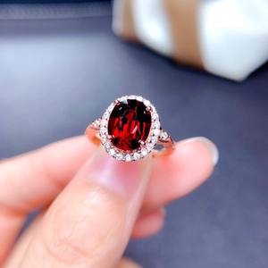 Rose gold ring featuring an oval red gemstone and diamonds, macro shot on a blurred background