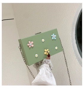 Close-up of green hard-shell chain bag featuring vibrant 3D floral daisy decorations