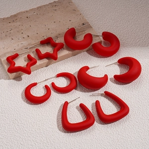 Five pairs of matte red acrylic C-shaped and star stud earrings set on a stone background