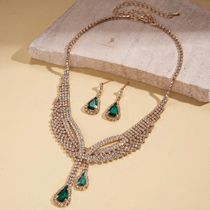 Detail of jewelry set with green teardrop stones and diamonds on textured stone