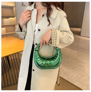 Green crescent handbag with woven texture and knotted handle shown with a beige coat
