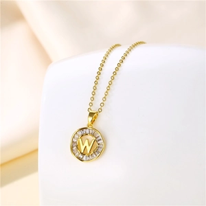 Detail of 18K gold letter W pendant with baguette zircon stones on beige silk