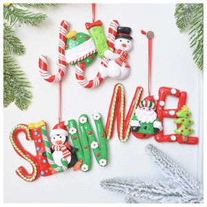 Close-up of JOY letter clay ornaments with snowman and santa on snowy cedar branches