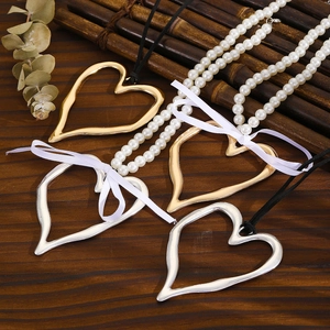 Détail de grands pendentifs en cœur creux avec chaînes de perles et cordons noirs sur bois