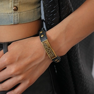 Close-up of leather bracelet with engraved brass plate and golden studs on denim cloth