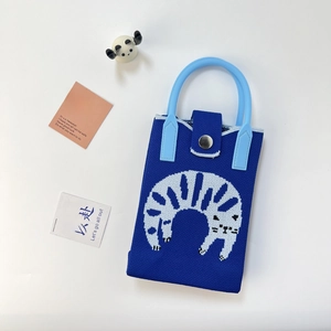 Detail of blue knitted phone bag featuring white cartoon pattern and magnetic closure
