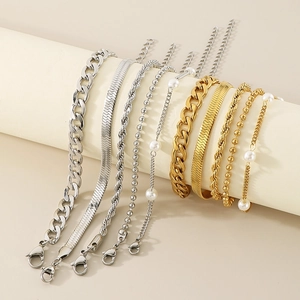 Close-up of golden and silver stacked bracelets with pearls and various chain link textures
