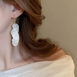 Detail shot of long tiered white shell-like disc drop earrings on a model