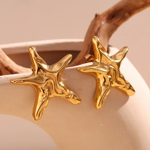 Close-up of gold starfish earrings with irregular texture on a ceramic background