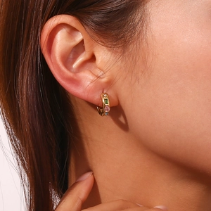 Détail d'une boucle d'oreille dorée 18K avec zircons colorés sur une oreille féminine