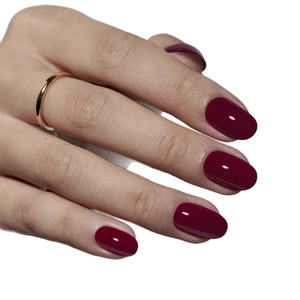 Faux ongles courts ovales rouge cerise brillant avec bague dorée sur la main du modèle