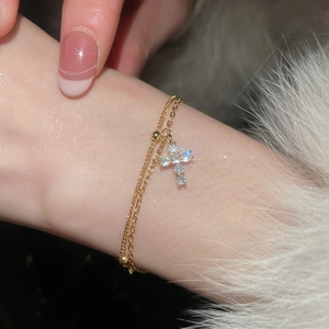 Close-up of gold double-layer bracelet featuring a sparkling zircon cross pendant