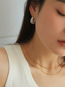 Close-up of silver hoop earrings and layered gold necklaces on a female model