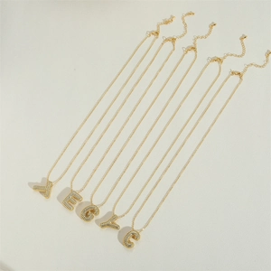 Detail of five gold necklaces with zircon-encrusted letters T E G Y C on sand background
