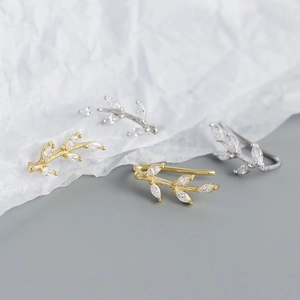 Close-up of gold and silver leaf-shaped ear cuffs with sparkling clear gemstones