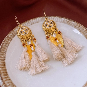 Détail des boucles d'oreilles fleurs dorées de style bohème avec pompons sur un plat en céramique