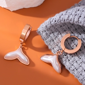 Rose gold fishtail hoop earrings with pearl shell inlay on orange background