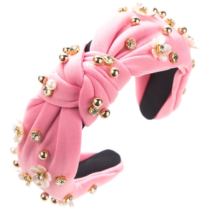 Détail d'un serre-tête en maille rose avec perles, billes dorées et fleurs en strass