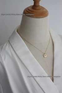 Detailed close-up of 18K gold plated square necklace with bee relief on white mother-of-pearl