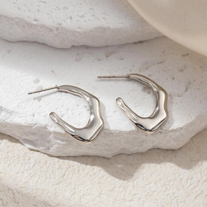 Macro shot of silver wavy irregular earrings on a textured stone and silk background